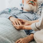 Close-up of older dying man holding his wife’s hands