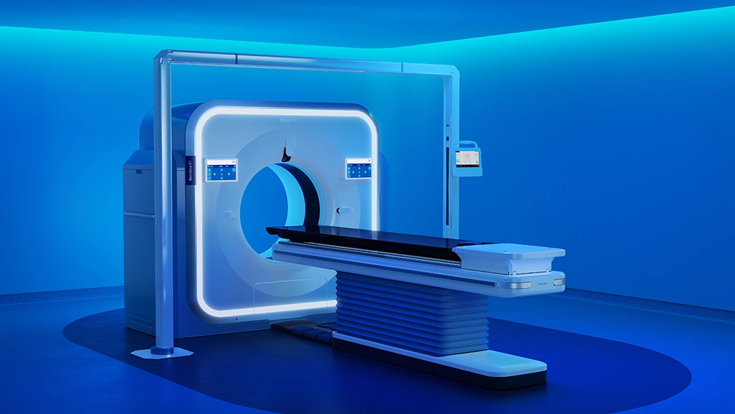 Philips CT scanner in a blue-lit radiology room with the patient table extended ready for imaging