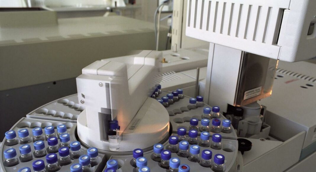 Automated laboratory analyzer with a circular rack of small vials with blue caps surrounding a central rotor core.