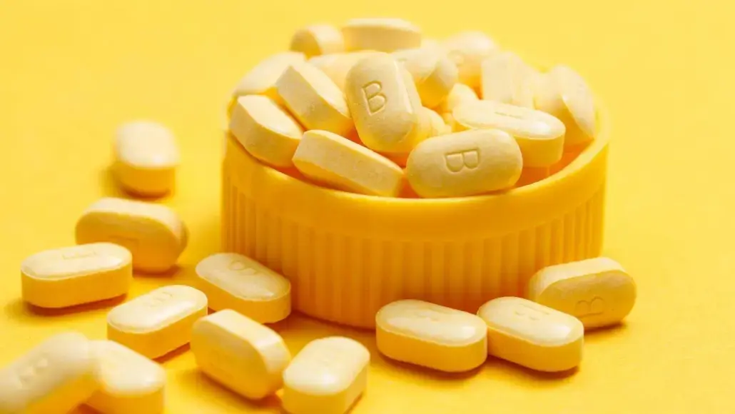 Pile of yellow oblong tablets spilling from a yellow bottle cap on a bright yellow background.