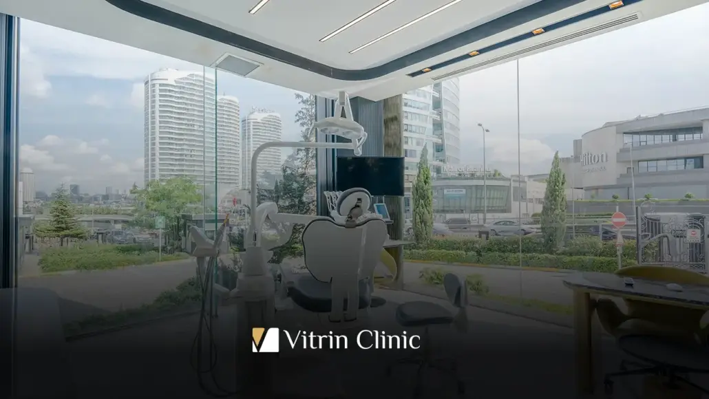 Modern dental treatment room with a patient chair, overhead lights, and dental equipment, seen through large glass windows onto a cityscape; Vitrin Clinic logo at bottom.