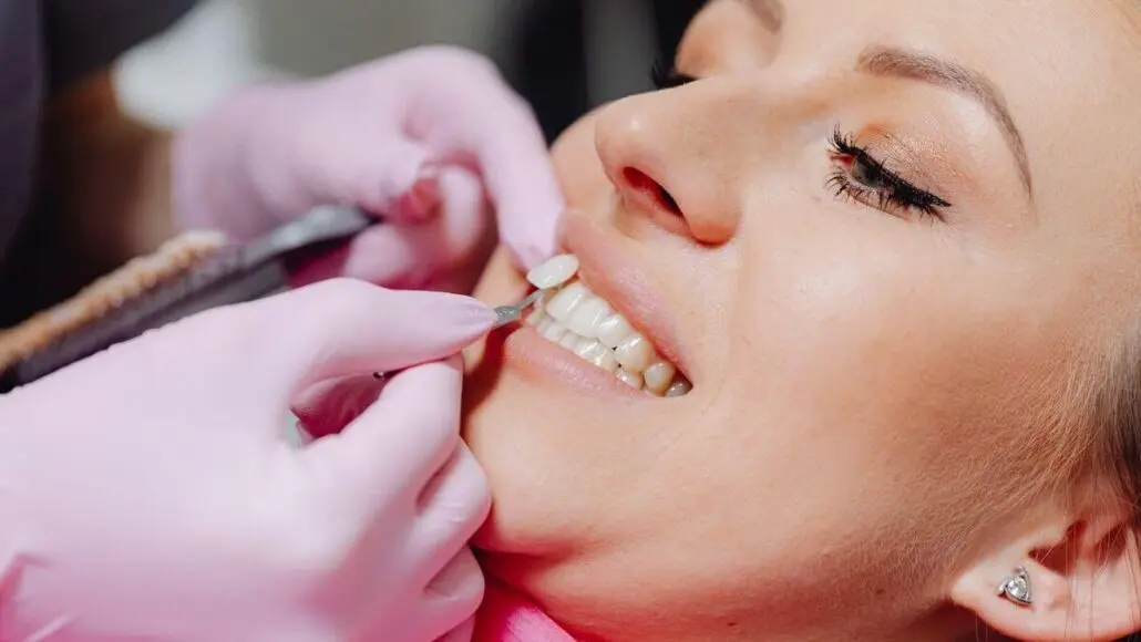 A dentist or hygienist wearing pink gloves works on a patient's teeth with dental instruments near the mouth (close-up).],